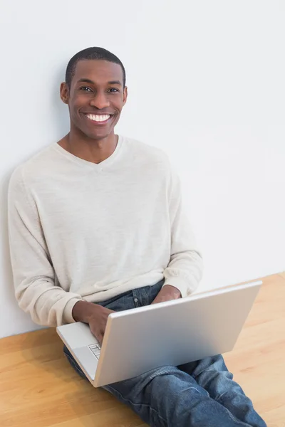 Glad afslappet afro ung mand ved hjælp af bærbar computer på gulvet - Stock-foto