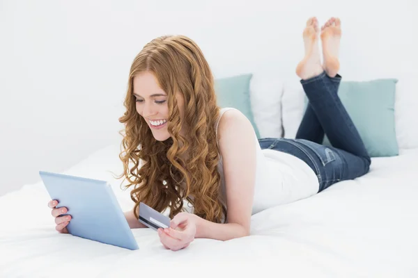 Chica pelirroja feliz con tablet PC y tarjeta de crédito en la cama —  Fotos de Stock