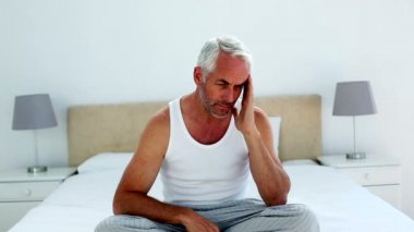 ressaca homem sentado do lado da sua cama e franzindo a testa