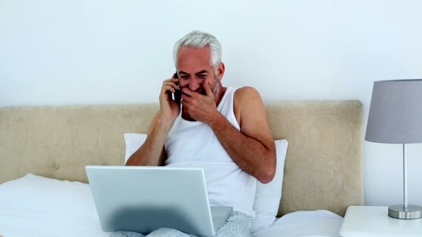 Сміється людина, використовуючи ноутбук, перебуваючи по телефону — стокове відео