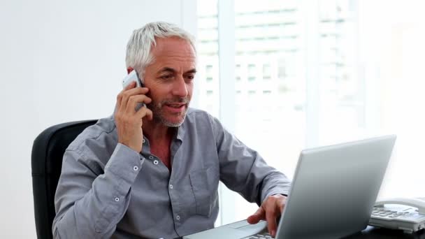 Příležitostné podnikatel pracuje na notebooku a povídali u stolu na telefonu — Stock video