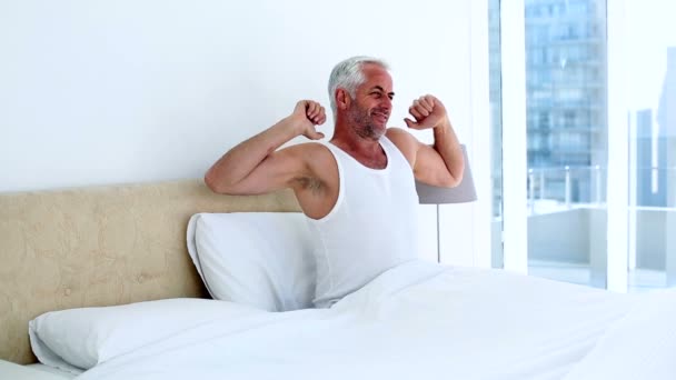 Sonriente hombre bostezando y estirándose sentado en la cama — Vídeo de stock