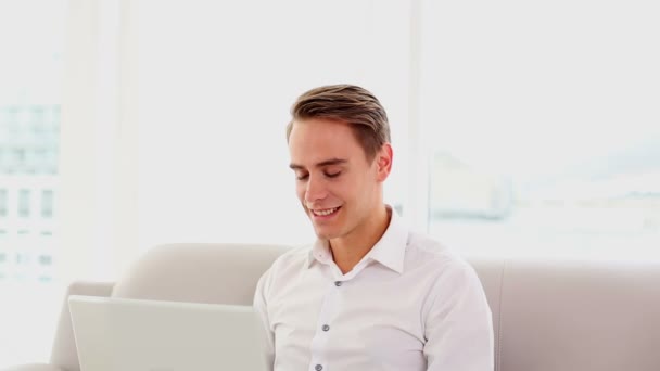 Juichende aantrekkelijke man met behulp van zijn laptop zittend op de Bank — Stockvideo