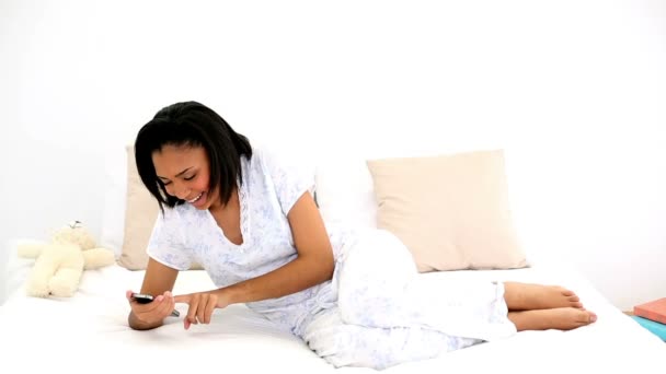 暗い髪の女性彼女のベッドの上に横たわる彼女のスマート フォンとメッセージング — ストック動画