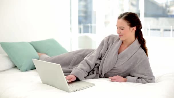 Peaceful brunette woman using her notebook wearing a bathrobe — Stock Video