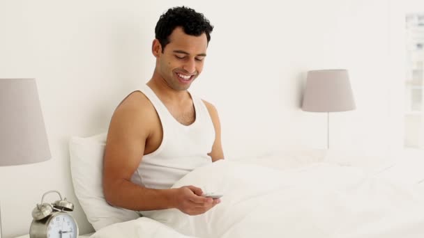 Vrolijke knappe man zittend op het bed texting — Stockvideo