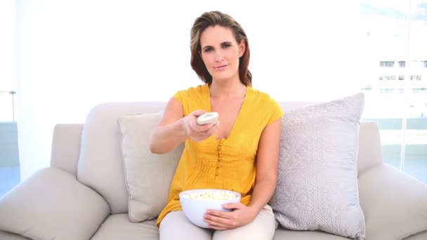 Улыбающаяся женщина смотрит телевизор с попкорном на диване — стоковое видео