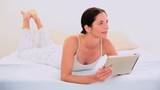 Приваблива брюнетка використовує свій цифровий планшет лежить на ліжку — стокове відео