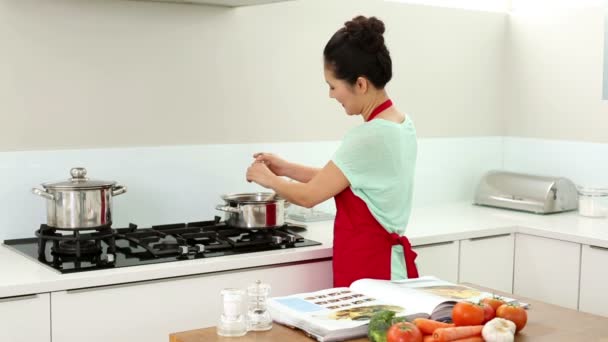 Lachende vrouw voorbereiden diner en de raadpleging van haar receptenboek — Stockvideo