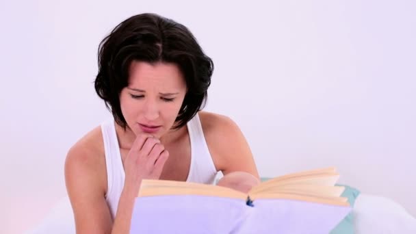 Pretty woman reading a book while sitting on her bed — Stock Video