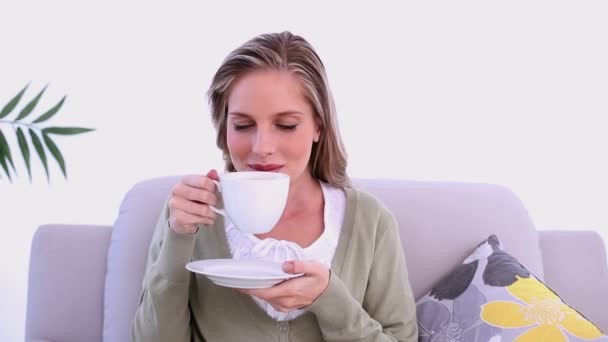 Mujer contenta bebiendo de la taza sentada en el sofá — Vídeos de Stock