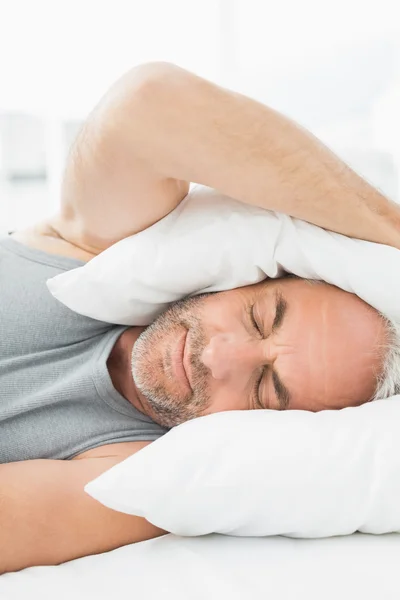 Ältere schläfrige Mann bedeckt Ohren mit Kissen im Bett — Stockfoto