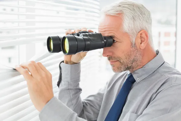 Empresario espiando con binoculares a través de persianas —  Fotos de Stock