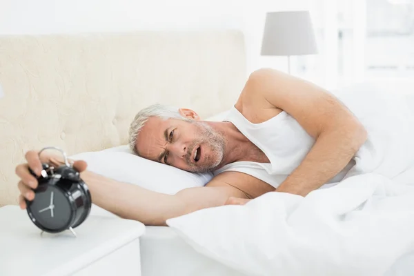 Reifer Mann reicht Zeiger an Wecker im Bett — Stockfoto