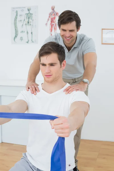 Male therapist assisting man with exercises in office — Stock Photo, Image