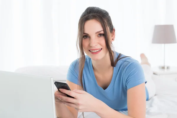 Mensajería de texto mujer mientras se utiliza el ordenador portátil en la cama — Foto de Stock