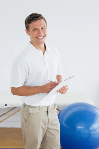 Spor salonunda hastane içinde clipboard ile erkek eğitmen gülümseyen — Stok fotoğraf