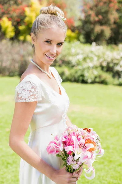 Pretty blonde bride holding lily bouquet smiling at camera — Stock Photo, Image