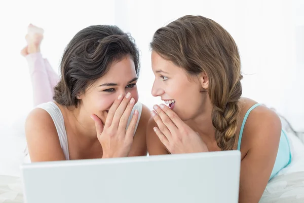 Felices amigas relajadas usando laptop en la cama —  Fotos de Stock