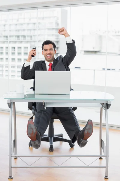 Businessman cheering in front of laptop at office desk — Stock Photo, Image