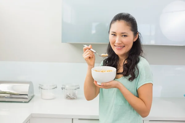 Smiling young woman eating cereals in kitchen — Stock Photo, Image