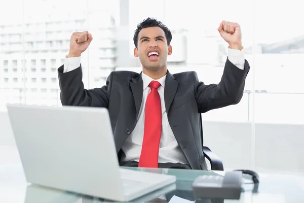 Businessman cheering in front of laptop at office desk — Stock Photo, Image