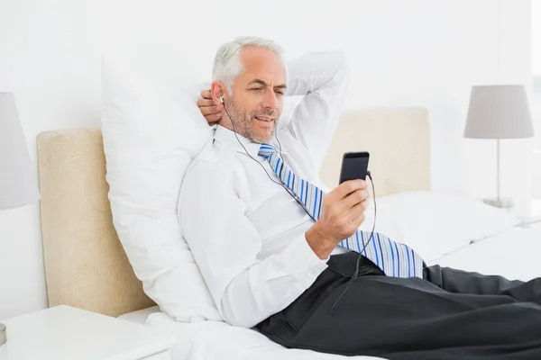 Biznesmen słuchania muzyki ze swojego telefonu w łóżku — Zdjęcie stockowe
