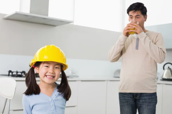 Nettes Mädchen mit hartem Hut und Vater, der Orangensaft in der Küche trinkt — Stockfoto