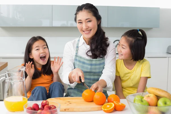 Femme avec gai deux filles coupant des fruits dans la cuisine — Photo