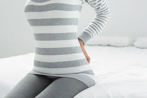 Mitten delen av en kvinna med rygg värk sitter i sängen — Stockfoto