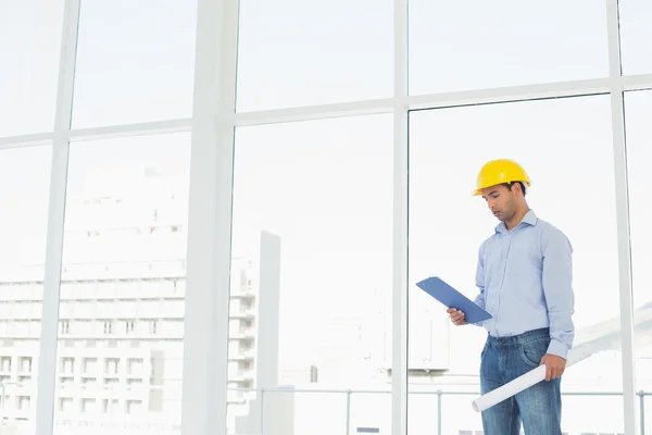 Handyman in hard hat with clipboard and blueprint in office — Stock Photo, Image