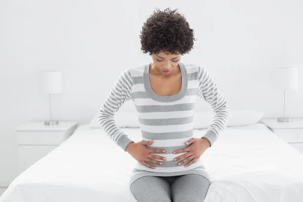 ベッドに座っている胃の痛みを持つカジュアルな女性 — ストック写真