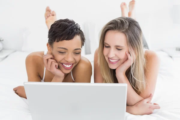 Happy relaxed friends using laptop in bed — Stock Photo, Image