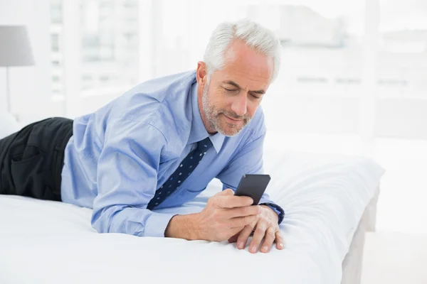 Sonriendo relajado hombre de negocios mensajería de texto en la cama —  Fotos de Stock