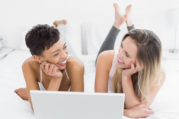 Amigos alegres do sexo feminino usando laptop na cama — Fotografia de Stock