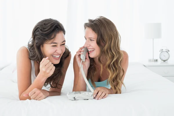 Ontspannen jonge vrouwelijke vrienden met behulp van telefoon in bed — Stockfoto
