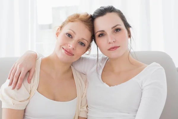 Smiling female friends with arm around in living room — Stok fotoğraf