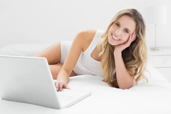 Souriant jeune femme en utilisant un ordinateur portable au lit — Photo