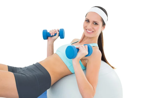 Mujer sonriente en forma haciendo ejercicio con pesas en la pelota de fitness —  Fotos de Stock