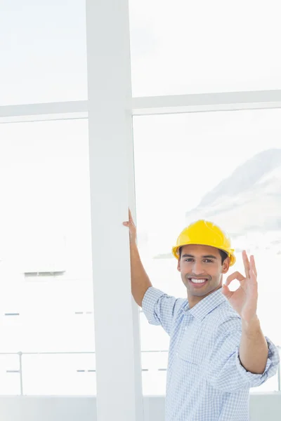 Handyman i gul hjälm gestikulerande okej tecken i office — Stockfoto