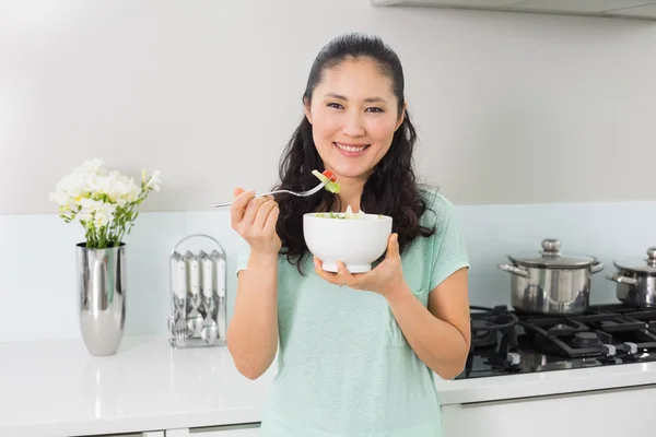 Smiling young woman with a bowl of salad in kitchen — Stock Photo, Image