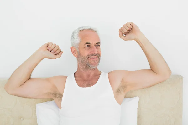 Mature smiling man stretching his arms in bed — Stock Photo, Image