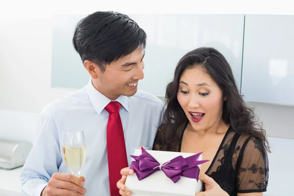 Shocked woman opening a gift box by man with champagne — Stock Photo, Image