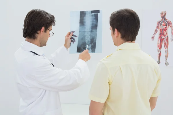 Médico masculino que explica a radiografia da coluna vertebral ao paciente — Fotografia de Stock