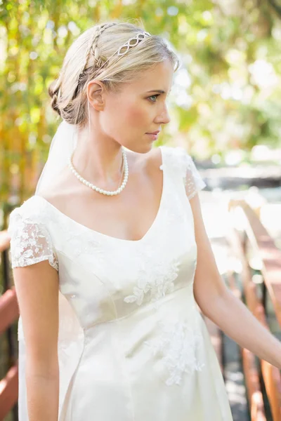 Contenuto sposa bionda in collana di perle in piedi su un ponte — Foto Stock