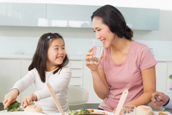 Menina e mãe comem comida na cozinha — Fotografia de Stock