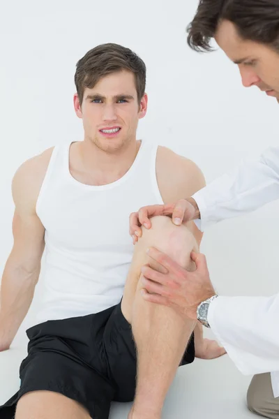 Displeased young man getting his knee examined — Stock Photo, Image