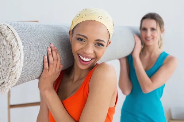 Female friends carrying rolled rug after moving in a house — Stock Photo, Image