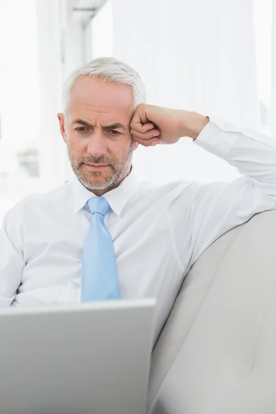 Mature businessman using laptop on sofa in living room — Stock Photo, Image