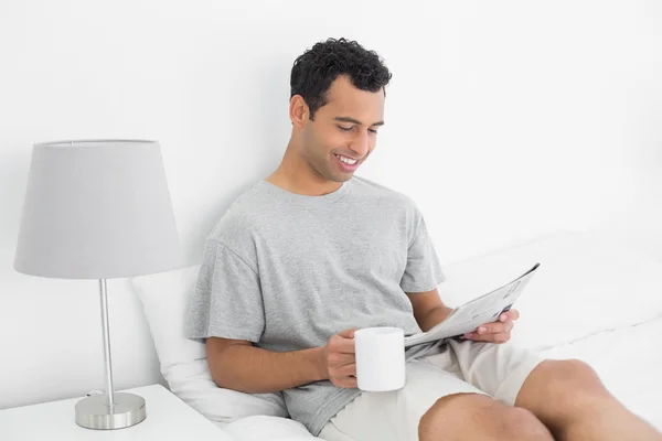 Расслабленный мужчина с газетой и кофейной чашкой в постели — стоковое фото